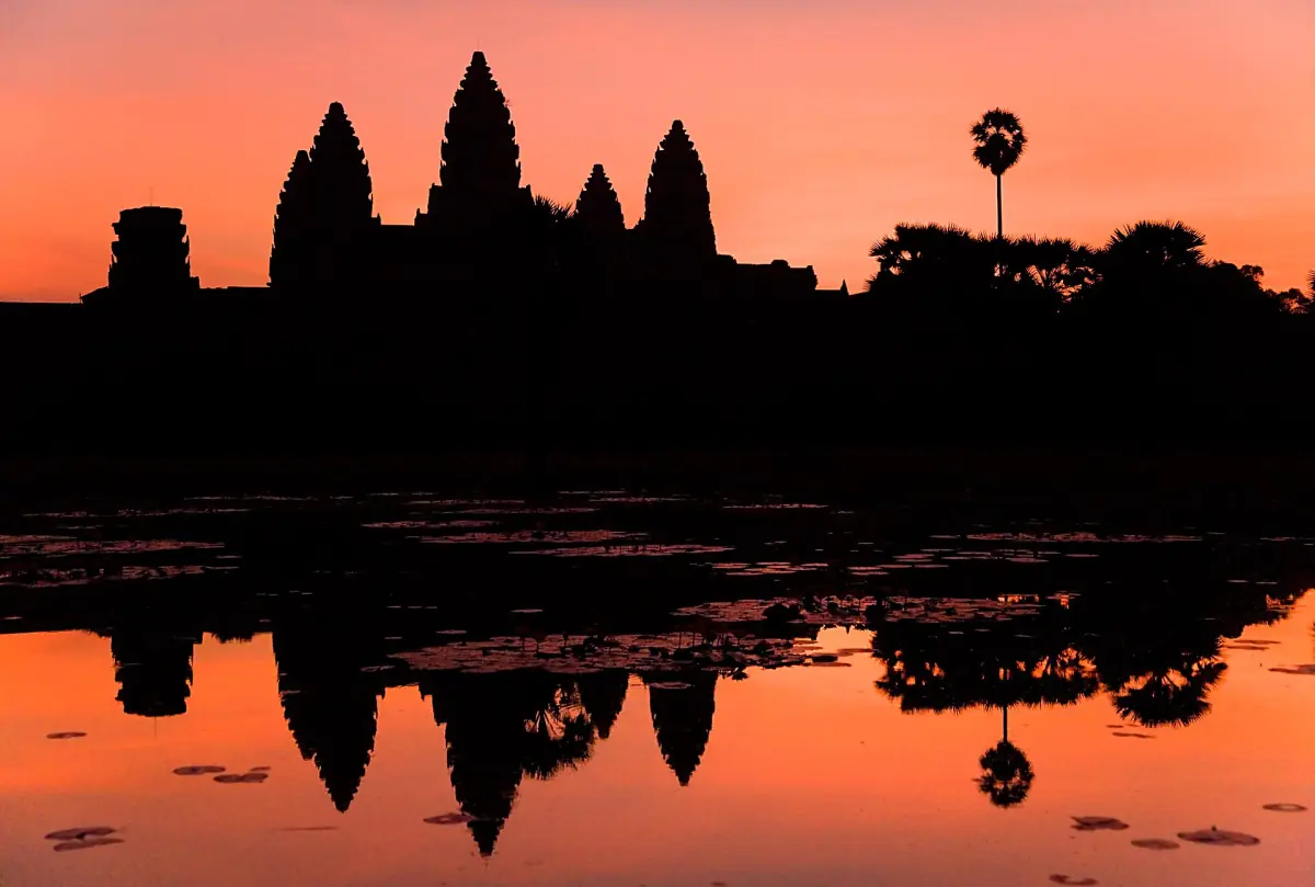 Angkor Wat silhouetted against an orange sky and reflected in the pond