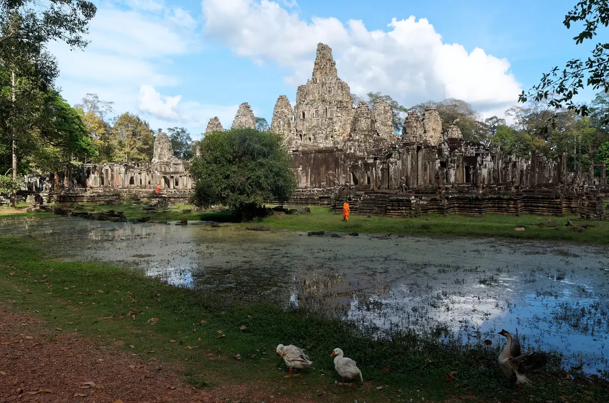 Bayon temple seen across a pond with clouds above the towers