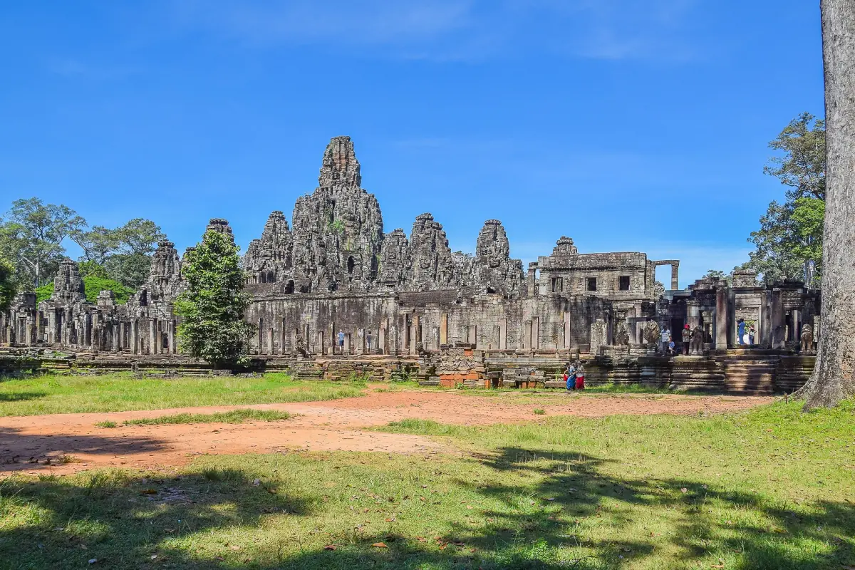Bayon temple towers rising behind grass and a dirt path on a sunny day