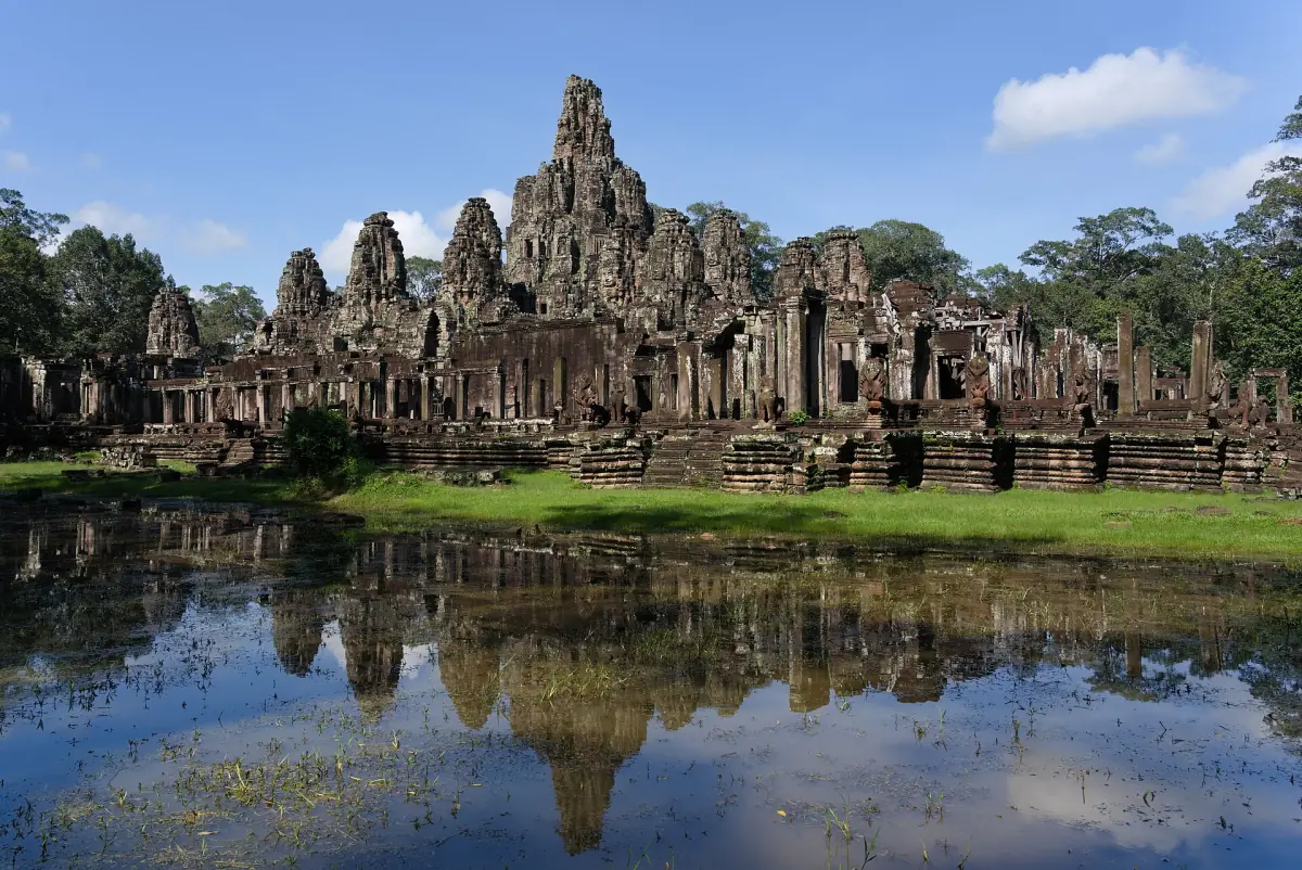 Bayon temple with its face towers reflected in the moat under a blue sky