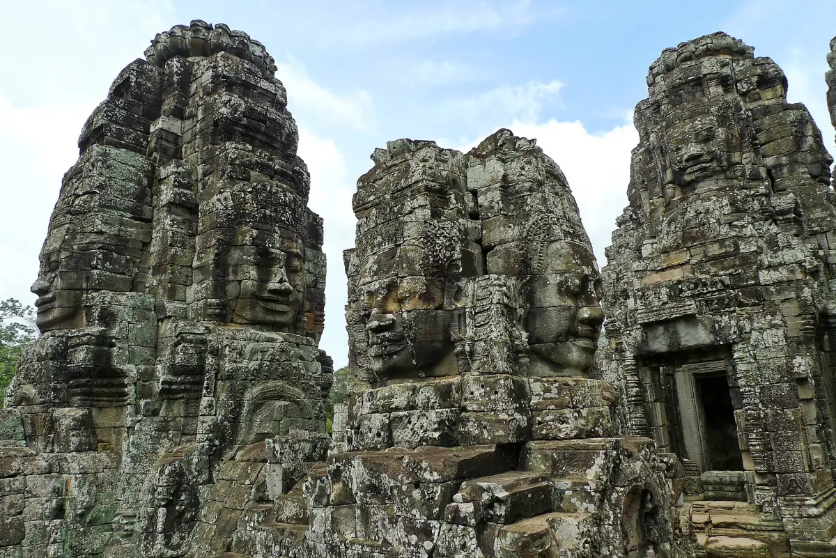 Three Bayon towers with large carved faces against a cloudy sky