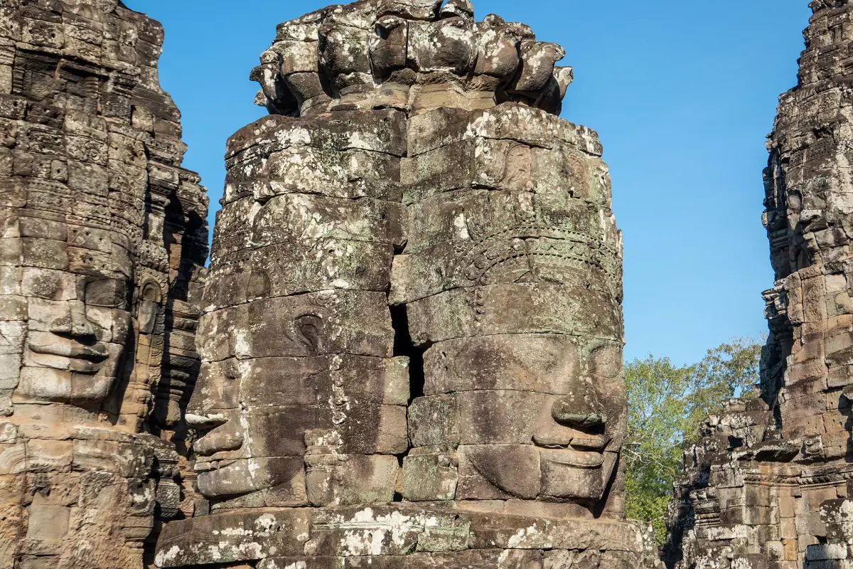 Sunlit faces carved on neighbouring Bayon towers under blue sky